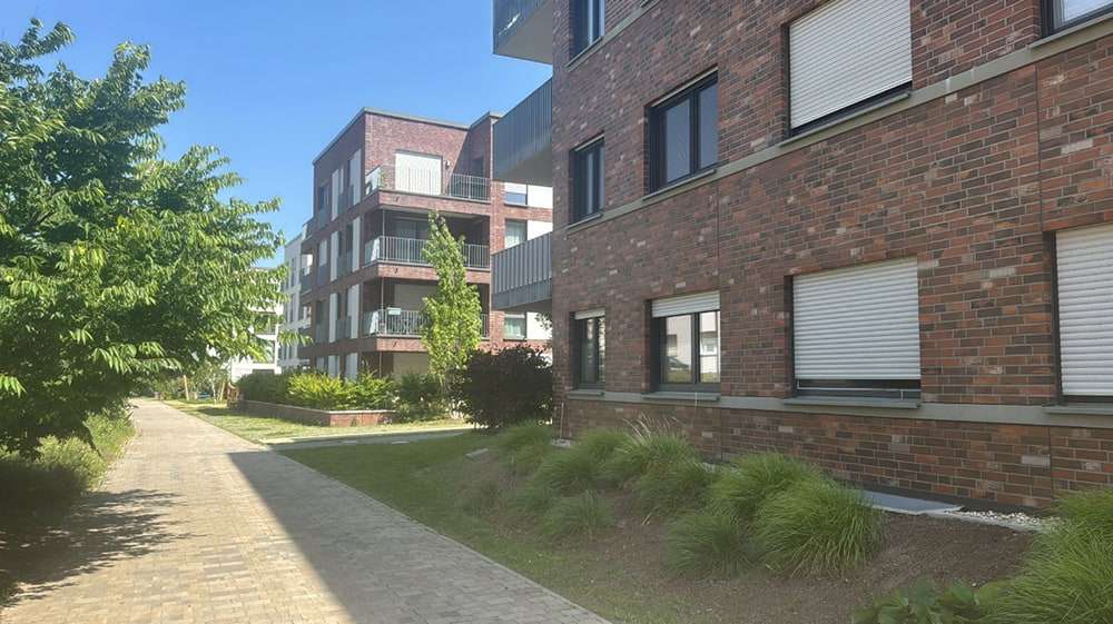 Gekehrter Gehweg mit gepflegtem Grünstreifen vor einer Wohnanlage